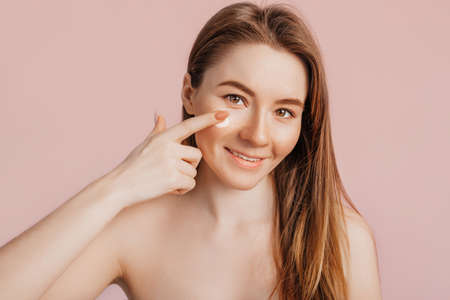 Girl make face beauty masks. Anti-wrinkle cream for the freshness of the skin around the eyes. Woman take care of youthful skin. Model laughing and having fun in spa on pink backgroundの写真素材