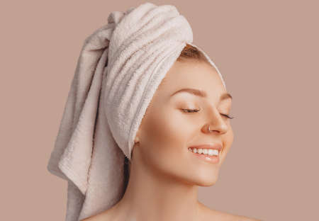 Beautiful sensual young girl with clean skin on a beige background with a mockup. Topless woman in a towel. The concept of spa treatments, natural beauty and care, youth, cream and mask, freshnessの写真素材