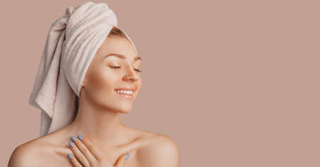 Beautiful sensual young girl with clean skin on a beige background with a mockup. Topless woman in a towel. The concept of spa treatments, natural beauty and care, youth, cream and mask, freshnessの写真素材