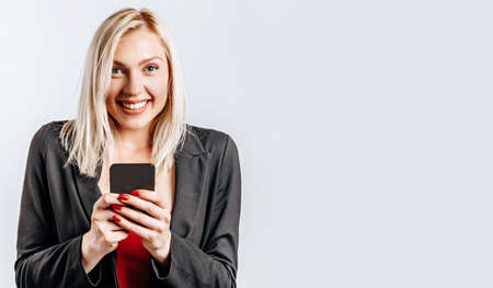 Beautiful young cute girl smiling and holding phone on gray isolated backgroundの写真素材