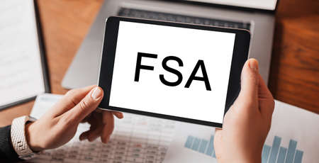 Man hands holding tablet with text FSA at workplace. Businessman working at desk with documentsの写真素材