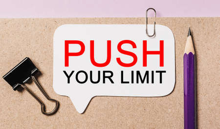 Text PUSH YOUR LIMIT on a white sticker with office stationery background. Flat lay on business, finance and development conceptの写真素材