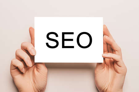 Female hands hold card paper with text SEO on a yellow background. Business and finance conceptの写真素材