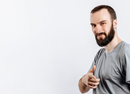 Portrait of cheerful young handsome man smiling looking at camera pointing finger forward on white background with space for advertising mock upの写真素材