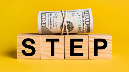 STEP with money on a yellow background. The concept of business, finance, credit, income, savings, investments, exchange, taxの写真素材