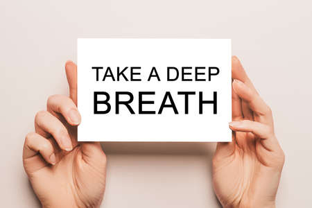 Female hands hold card paper with text Take a deep breath on a yellow background. Business and finance conceptの写真素材
