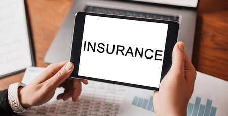 Man hands holding tablet with text INSURANCE at workplace. Businessman working at desk with documentsの写真素材