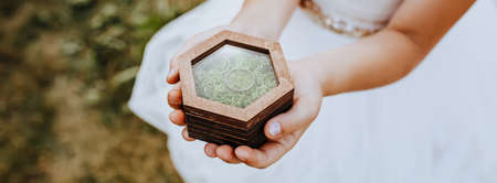 A child holds with his hands two wedding rings in a wooden box with a plant mossの写真素材