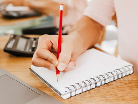 Man writes business information in notebook at workplace in office with calculator and laptopの写真素材