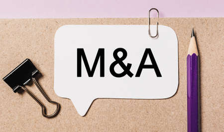 Text M and A on a white sticker with office stationery background. Flat lay on business, finance and development conceptの写真素材
