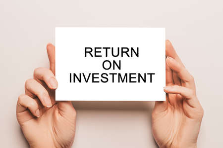 Female hands hold card paper with text Return on Investment on a yellow background. Business and finance conceptの写真素材