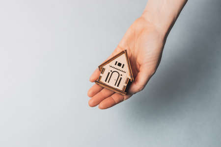 Woman holding a wooden house with her hands with the sun on a light blue background. Sweet homeの写真素材