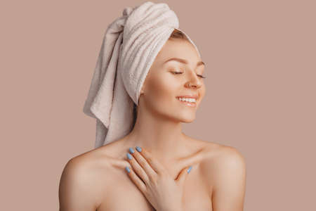 Beautiful sensual young girl with clean skin on a beige background with a mockup. Topless woman in a towel. The concept of spa treatments, natural beauty and care, youth, cream and mask, freshnessの写真素材