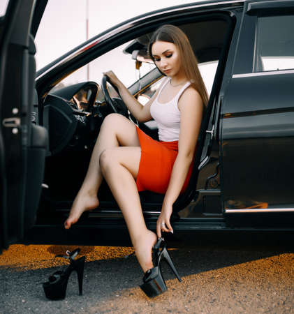 Beautiful young girl driving a car in the evening in the sunset sun on an empty parking lotの写真素材