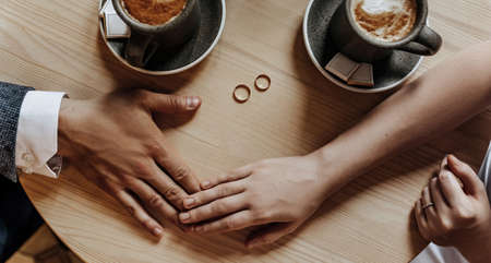 Man and woman couple of newlyweds hold hands with rings in a cafe with a cup of coffee. The bride and groom are in loveの写真素材