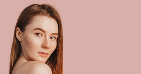 Beautiful sensual young girl with clean skin on a pink background with a mockup. Topless woman in a towel. The concept of spa treatments, natural beauty and care, youth, cream and mask, freshnessの写真素材