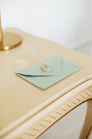 Two wedding rings lie on an invitation with gold backgroundの写真素材