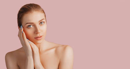 Beautiful sensual young girl with clean skin on a pink background with a mockup. Topless woman in a towel. The concept of spa treatments, natural beauty and care, youth, cream and mask, freshnessの写真素材