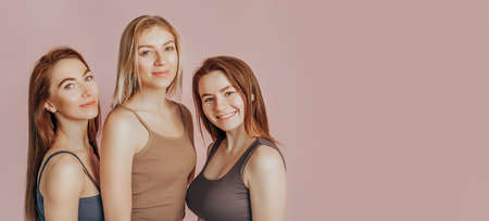 Three girls in comfortable home clothes together on a pink background. Women smile and have fun. The concept of spa treatments, natural beauty and care, youth, cream and mask, freshness, friendshipの写真素材