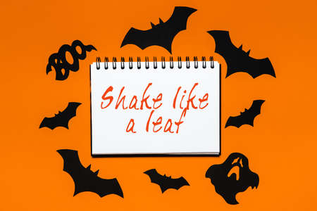 Happy halloween holiday concept. Notepad with text Shake like a leaf on white and orange background with bats, pumpkins and ghostsの写真素材