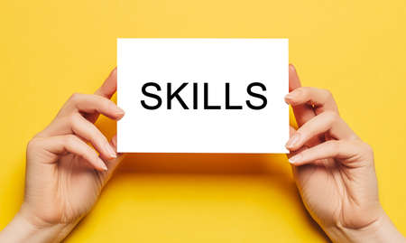 Female hands hold card paper with text SKILLS on a yellow background. Business and finance conceptの写真素材