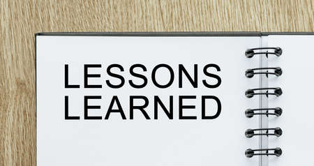 Notepad with text LESSONS LEARNED on wooden deskt. Business and finance conceptの写真素材
