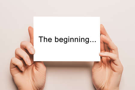 Female hands hold card paper with text The beginning on a yellow background. Business and finance conceptの写真素材