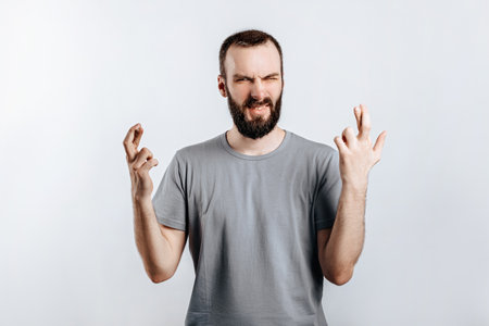 Handsome young man frown and cross fingers in hope on white background with space for advertising mock upの写真素材