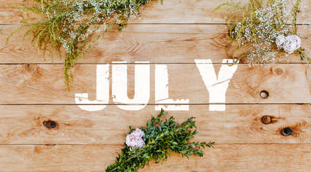 Text july on light wood decorated with plants and flowers. Wooden texture background mockup backgroundの写真素材