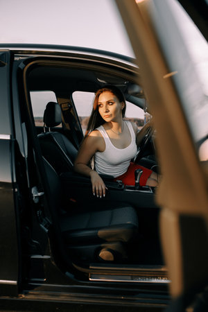 Beautiful young girl driving a car in the evening in the sunset sun on an empty parking lot