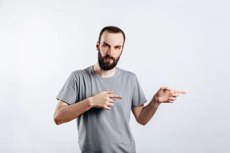 Portrait of cheerful young handsome man smiling looking at camera pointing finger to the side on white background with space for advertising mock upの写真素材