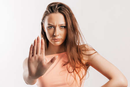 Stop. Enough. Young beautiful girl stretches out her hand to the camera to stop the effect. Woman with fashion orange top on an isolated gray background. Bad events, despair and threatの写真素材