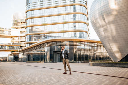 Handsome man with glasses with a smartphone on the street of a big city. Businessman talking on the phone on urban backgroundの写真素材