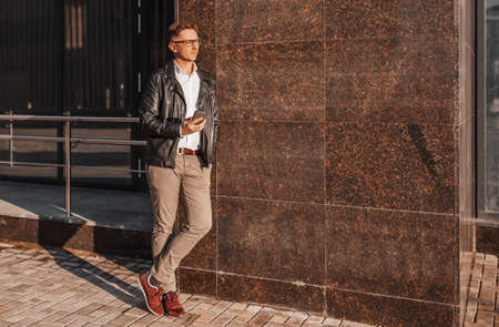 Handsome man with glasses with a smartphone on the street of a big city. Businessman talking on the phone on urban backgroundの写真素材