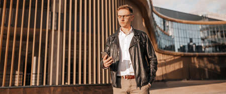 Handsome man with glasses with a smartphone on the street of a big city. Businessman talking on the...