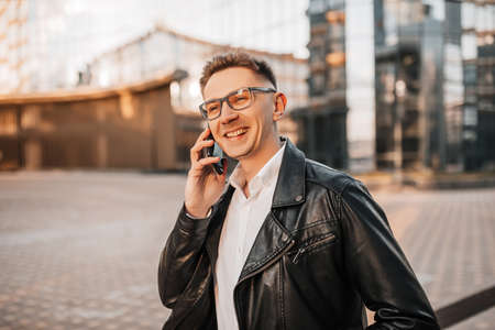 Handsome man with glasses with a smartphone on the street of a big city. Businessman talking on the phone on urban backgroundの写真素材