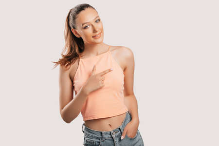 Portrait of a smiling girl pointing finger to the side at on a white isolated background. Positive woman points to an idea, a place for advertisingの写真素材