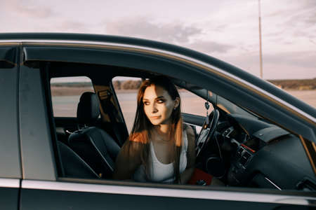 Beautiful young girl driving a car in the evening in the sunset sun on an empty parking lotの写真素材