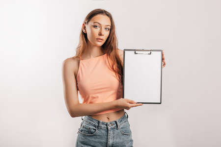 Girl student points to the sheet. Beautiful young business woman holds a clipboard with mockup blank space isolated on gray background. Study and business concept. Online learning coverの写真素材