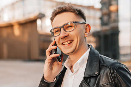 Handsome man with glasses with a smartphone on the street of a big city. Businessman talking on the phone on urban backgroundの写真素材