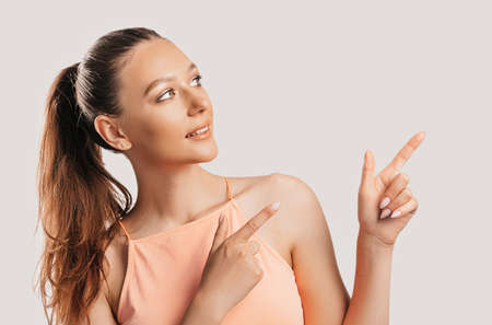 Portrait of a smiling girl pointing finger to the side at on a white isolated background. Positive woman points to an idea, a place for advertisingの写真素材