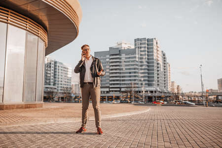 Handsome man with glasses with a smartphone on the street of a big city. Businessman talking on the phone on urban backgroundの写真素材