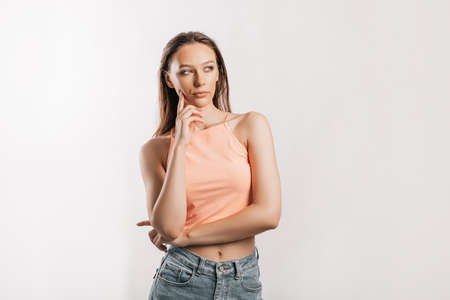 Beautiful young girl unhappy frown and thinks on gray isolated background. Serious woman looks to the side and holds hand to faceの写真素材