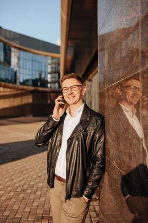 Handsome man with glasses with a smartphone on the street of a big city. Businessman talking on the phone on urban backgroundの写真素材