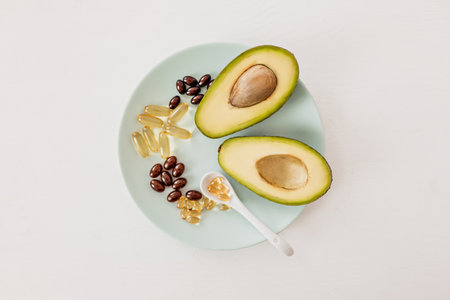 Health care and diet concept. Avocado and fish oil in capsules for vitamin D and omega-3 fatty acids in a plate on a white backgroundの写真素材