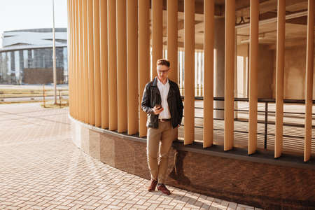 Handsome man with glasses with a smartphone on the street of a big city. Businessman talking on the phone on urban backgroundの写真素材