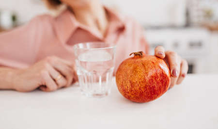 The girl is holding a pomegranate and water in the kitchen. Health care concept, dietの写真素材