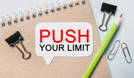 Text PUSH YOUR LIMIT on a white sticker with office stationery background. Flat lay on business, finance and development conceptの写真素材