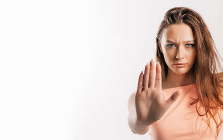 Stop. Enough. Young beautiful girl stretches out her hand to the camera to stop the effect. Woman with fashion orange top on an isolated gray background. Bad events, despair and threatの写真素材