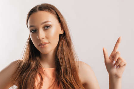 Portrait of a smiling girl pointing finger to the side at on a white isolated background. Positive woman points to an idea, a place for advertisingの写真素材